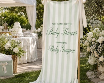 May include: A vertical fabric banner with light green and white vertical stripes, suspended from a wooden frame with white ribbons. The text reads: WELCOME TO THE Baby Shower HONORING Baby Grayson in dark green script and block lettering.