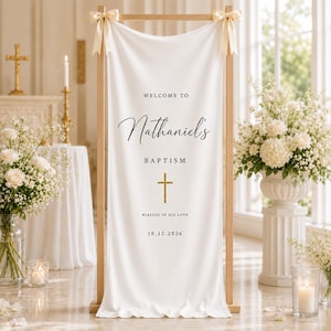 Pode incluir: Uma faixa de tecido branco suspensa numa moldura de madeira clara com fitas cor de creme nos cantos superiores. A faixa apresenta o texto preto "WELCOME TO Nathaniel's BAPTISM", um ícone de cruz dourada e a data "10.12.2026" em preto.