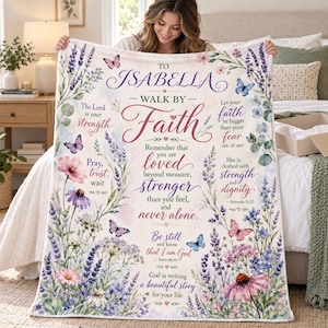 May include: A white fleece blanket featuring a floral design with lavender, pink, and blue flowers, green leaves, and butterflies. The text reads: To Isabella, Walk by Faith, The Lord is your strength, Let your faith be bigger than your fear.