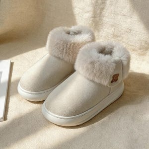 May include: A pair of cream-colored, plush slippers with a faux fur trim. The slippers have a thick, white sole and a small decorative emblem on the side. The soft, cozy design suggests comfort and warmth, perfect for indoor wear.