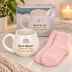 以下が含まれることがあります： 積み重ねられた本のグラフィックと茶色の文字でGood Books Warm Tea Fuzzy Socksと書かれた丸みを帯びた白いセラミックマグカップ。柔らかいライトピンクのふわふわした靴下と、お揃いのギフトボックスがセットになっています。
