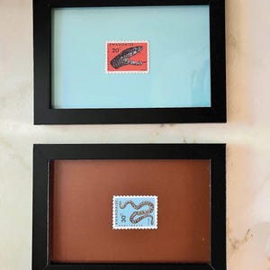 Peut inclure: Deux timbres-poste encadrés avec des illustrations de serpents. Un timbre rouge montre un serpent et le texte "20". L'autre timbre bleu montre un serpent et le texte "30". Les deux timbres sont dans des cadres noirs.