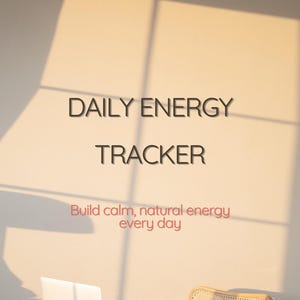 Op de afbeelding: Een minimalistische werkruimte met een laptop, een rieten stoel en een glas. De muur toont de tekst "DAILY ENERGY TRACKER" en "Build calm, natural energy every day" in zwart en rood.