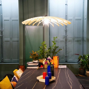 May include: A light-colored wooden pendant lamp with a circular, petal-like structure hangs above a dark table. The lamp features thin, curved slats radiating from a central point, illuminated by a single light bulb at its core.