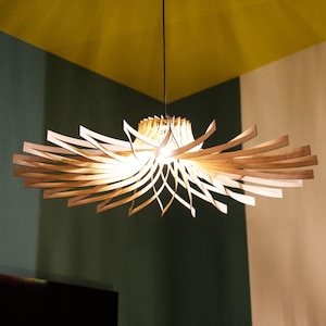 Könnte beinhalten: Eine moderne Holz-Pendelleuchte mit einem einzigartigen, geschichteten Design. Das Licht hat einen zentralen Kern mit strahlenden, gebogenen Holzlamellen, die ein warmes, einladendes Leuchten erzeugen. Die Leuchte hängt an einem schwarzen Kabel in einem Raum.