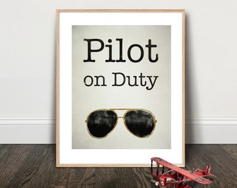 Pode incluir: Uma impressão emoldurada com o texto "Pilot on Duty" e um par de óculos de sol aviador em preto e dourado.