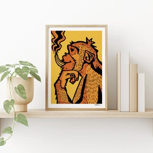 May include: Framed art print featuring a stylized illustration of a monkey smoking a banana. The artwork is in shades of orange and black against a yellow background. The print is displayed on a wooden shelf with a potted plant and books.