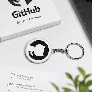 Pode incluir: Um chaveiro NFC branco e preto com o logotipo do GitHub, uma silhueta de gato dentro de um círculo. O chaveiro está preso a um porta-chaves prateado. Uma caixa branca com o logotipo e o texto do GitHub está no fundo.