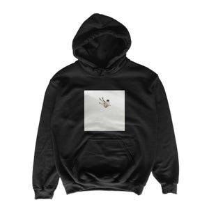 May include: Black hooded sweatshirt with a front pocket and drawstring hood. The sweatshirt features a square graphic on the chest depicting a person falling. The graphic is in shades of white and gray.