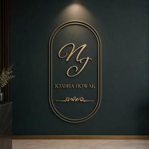 May include: A wall-mounted sign featuring a gold-coloured oval frame with the stylized script initials NJ, the name JOANNA NOWAK in capital letters, and a decorative flourish element centred on a dark teal wall surface.