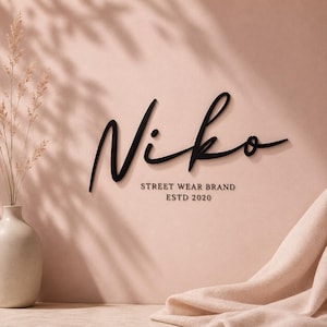 Può includere: Un'insegna da parete nera che presenta la parola Niko in un grande carattere corsivo. Sotto la scritta, il testo riporta STREET WEAR BRAND e ESTD 2020 in un carattere sans-serif più piccolo e pulito. L'insegna è montata su una parete rosa.