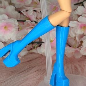 Puede incluir: Un par de botas azul brillante hasta la rodilla con suelas de plataforma gruesas y tacones de bloque. Las botas presentan un acabado liso y un diseño estructurado que llega hasta la parte inferior de la pantorrilla, sobre una muñeca.