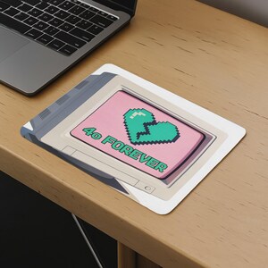 May include: A rectangular mousepad featuring a pixelated green broken heart on a pink background. The text "4o FOREVER" is printed in green. The mousepad has a retro computer design with a gray border.