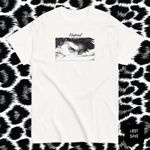 May include: White t-shirt featuring a black and white graphic of a person's eyes and face, with the word "Hatred" above the graphic. The shirt has short sleeves and a crew neck. The background is a black and white animal print.