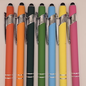 Könnte beinhalten: Eine Sammlung von sieben farbenfrohen Stift-Stiften. Die Stifte sind in den Farbtönen Orange, Grün, Blau und Pink gehalten, mit silbernen Akzenten und schwarzen Spitzen. Jeder Stift hat ein schlankes, modernes Design.