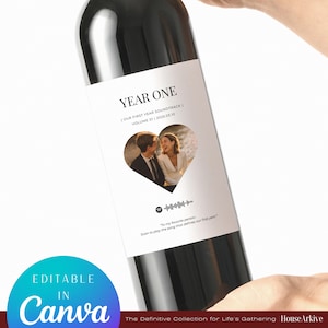 May include: A wine bottle with a personalised label. The label reads "YEAR ONE" and "OUR FIRST YEAR SOUNDTRACK". A heart-shaped photo of a couple is in the centre. The label also includes a Spotify code and the text "EDITABLE IN Canva".
