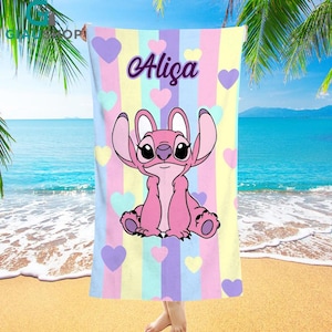 A colorful towel featuring a cartoon character from the Disney movie Lilo and Stitch, with the name "Alica" printed on it. The towel is displayed on a beach with palm trees and a blue ocean in the background.