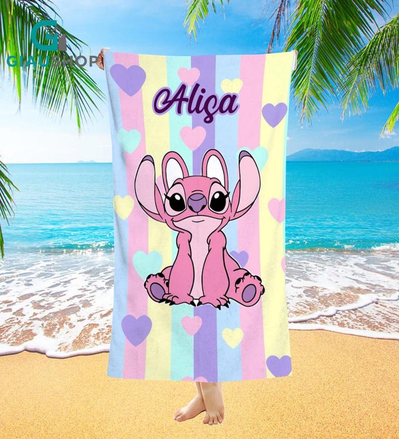 A colorful towel featuring a cartoon character from the Disney movie Lilo and Stitch, with the name "Alica" printed on it. The towel is displayed on a beach with palm trees and a blue ocean in the background.