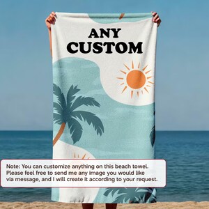 A person is holding a beach towel with a tropical design, including palm trees and a sun, against a backdrop of the ocean.