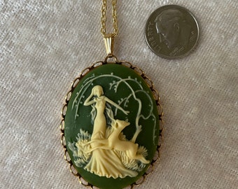 Può includere: Una collana con catena dorata con un ciondolo a cammeo verde che raffigura una donna bianca e un cerbiatto in una scena di bosco.