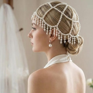 May include: A pearl headpiece with a grid design and dangling strands, paired with matching pearl earrings. The headpiece is worn with a white halter top. The woman's hair is styled in a low bun.