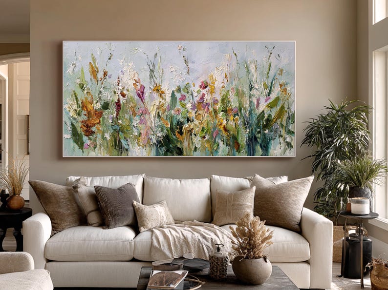 Pu&ograve; includere: Dipinto floreale astratto in una cornice bianca. L'opera presenta un vivace mix di colori, tra cui arancione, giallo, rosa e verde, che raffigurano un campo di fiori selvatici. Il dipinto &egrave; esposto sopra un divano bianco.