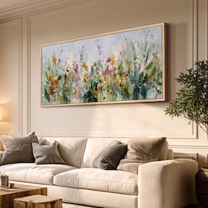 Pu&ograve; includere: Un dipinto floreale astratto in una cornice di legno chiaro &egrave; appeso sopra un divano color crema. L'opera presenta un mix di pennellate verdi, gialle, arancioni e viola. La stanza &egrave; decorata con toni neutri, un tavolino di legno e una pianta in vaso.