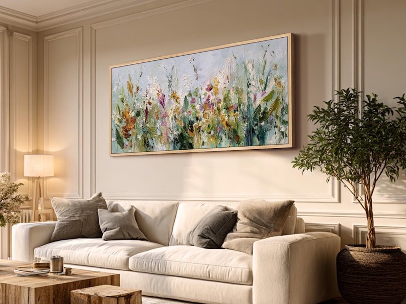 Pu&ograve; includere: Un dipinto floreale astratto in una cornice di legno chiaro &egrave; appeso sopra un divano color crema. L'opera presenta un mix di pennellate verdi, gialle, arancioni e viola. La stanza &egrave; decorata con toni neutri, un tavolino di legno e una pianta in vaso.