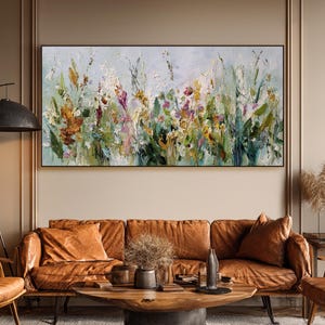 Pu&ograve; includere: Dipinto floreale astratto in una cornice nera. L'opera presenta un vivace mix di colori, tra cui verde, giallo, arancione e viola, che raffigurano un campo di fiori selvatici. Il dipinto &egrave; appeso sopra un divano in pelle marrone.
