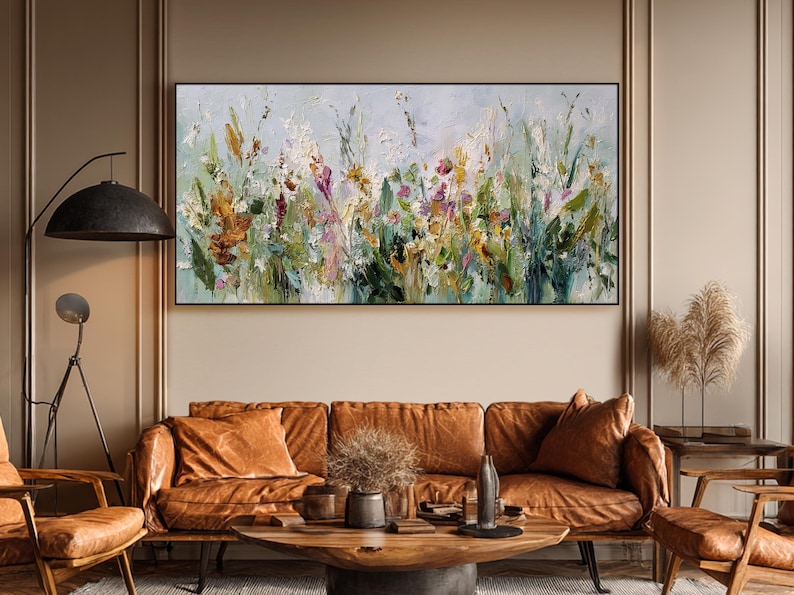 Pu&ograve; includere: Dipinto floreale astratto in una cornice nera. L'opera presenta un vivace mix di colori, tra cui verde, giallo, arancione e viola, che raffigurano un campo di fiori selvatici. Il dipinto &egrave; appeso sopra un divano in pelle marrone.