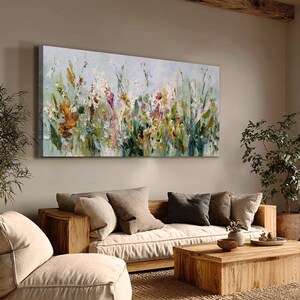 Pu&ograve; includere: Dipinto floreale astratto su tela, con una variet&agrave; di fiori selvatici nei toni dell'arancione, giallo, viola e verde. L'opera d'arte &egrave; esposta sopra un divano e un tavolino di legno, creando un ambiente caldo.