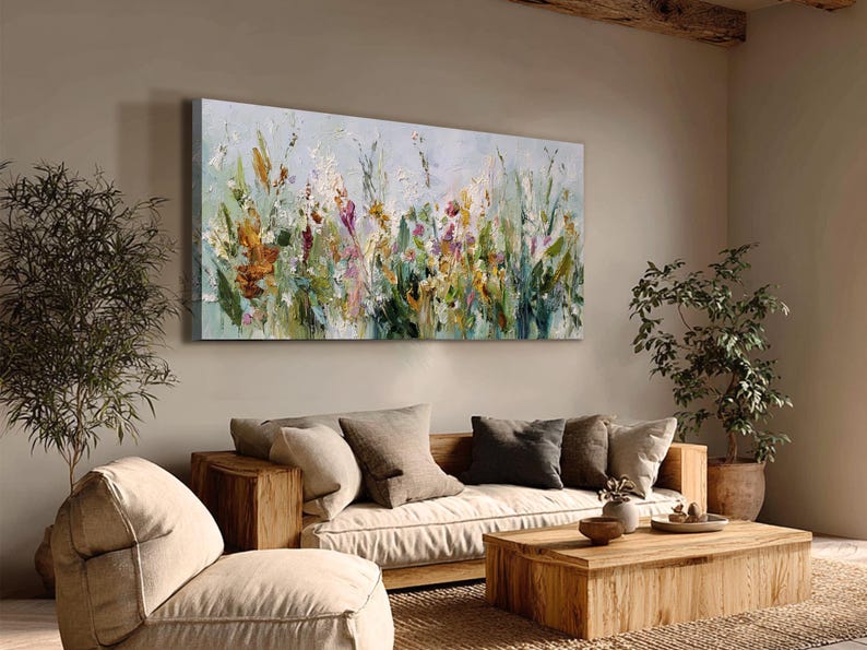 Pu&ograve; includere: Dipinto floreale astratto su tela, con una variet&agrave; di fiori selvatici nei toni dell'arancione, giallo, viola e verde. L'opera d'arte &egrave; esposta sopra un divano e un tavolino di legno, creando un ambiente caldo.