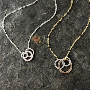 Peut inclure: Deux colliers en argent avec des pendentifs circulaires texturés. Les colliers sont superposés sur une surface texturée grise.