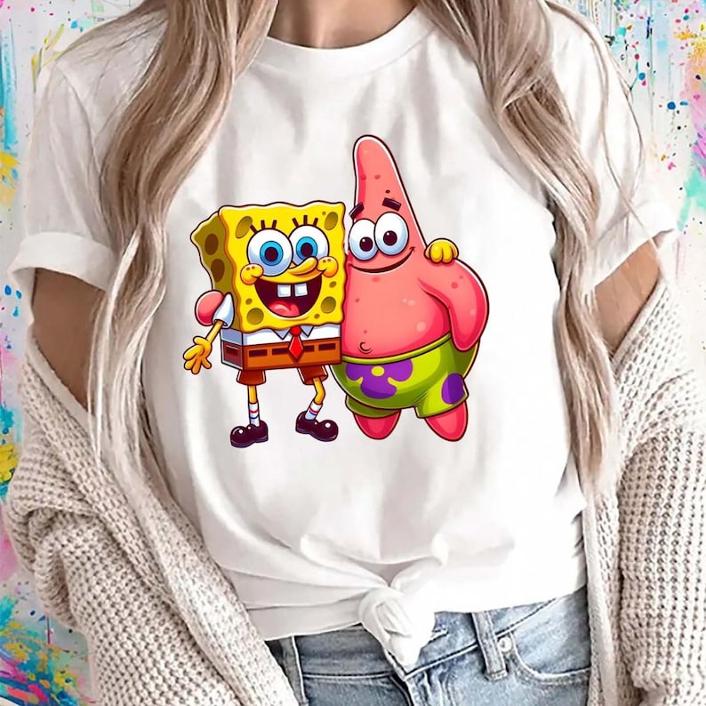 Puede incluir: Camiseta blanca con un gr&aacute;fico de dibujos animados de Bob Esponja y Patricio Estrella. Bob Esponja es amarillo con una corbata roja y pantalones cortos marrones. Patricio es rosa con pantalones cortos verdes. El dise&ntilde;o est&aacute; centrado.