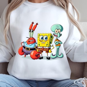 Puede incluir: Sudadera blanca con un gr&aacute;fico colorido de Bob Esponja, Calamardo Tent&aacute;culos y Don Cangrejo. Los personajes de dibujos animados est&aacute;n en un estilo vibrante. La sudadera es una prenda casual y c&oacute;moda.