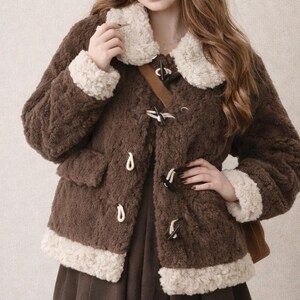 May include: A brown, textured coat with a cream-coloured collar and trim, featuring toggle closures. The coat is paired with a matching beret and a brown skirt. The overall style is vintage-inspired and cosy.