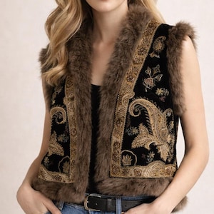 May include: A black vest with brown faux fur trim and gold embroidery. The vest features a paisley design and is worn with a black belt and blue jeans. The vest is sleeveless.