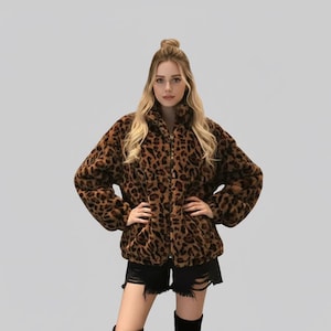 Puede incluir: Chaqueta con estampado de leopardo marr&oacute;n y negro, con cuello alto y cierre de cremallera. La chaqueta est&aacute; hecha de un material suave y afelpado y tiene mangas largas. La modelo lleva un pantal&oacute;n corto negro y botas negras.