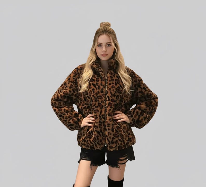 Puede incluir: Chaqueta con estampado de leopardo marr&oacute;n y negro, con cuello alto y cierre de cremallera. La chaqueta est&aacute; hecha de un material suave y afelpado y tiene mangas largas. La modelo lleva un pantal&oacute;n corto negro y botas negras.