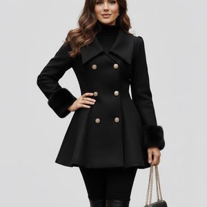 May include: A black double-breasted coat with gold buttons and faux fur cuffs. The coat has a flared skirt and a wide collar. A black purse with a gold chain strap is held in the hand.