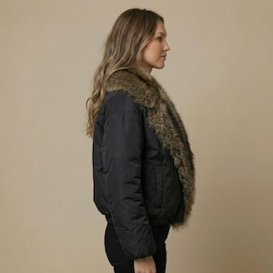 Könnte beinhalten: Schwarze Bomberjacke mit einem Kunstfellkragen. Die Jacke hat ein gestepptes Design und einen gerippten Saum und Bündchen. Der Kunstfellkragen ist eine Mischung aus braunen und beigen Farben. Die Jacke wird von der Seite gezeigt.