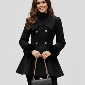 May include: A black double-breasted coat with gold buttons and faux fur cuffs. The coat has a flared skirt and a wide collar. A black purse with a gold chain is held in the hands.