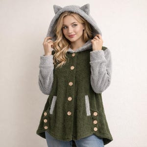 Może przedstawiać: Zielona kurtka z kapturem z szarymi rękawami i kapturem z uszami kota. Kurtka ma drewniane guziki i kieszenie. Miękki, pluszowy materiał zapewnia przytulny wygląd. Projekt jest przeznaczony dla wygody.