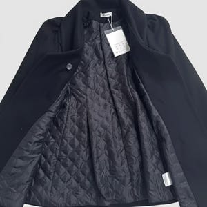 May include: A black coat with a quilted lining, open to display the interior. The coat has a classic collar and a single button closure. A white tag hangs from the inside of the coat.