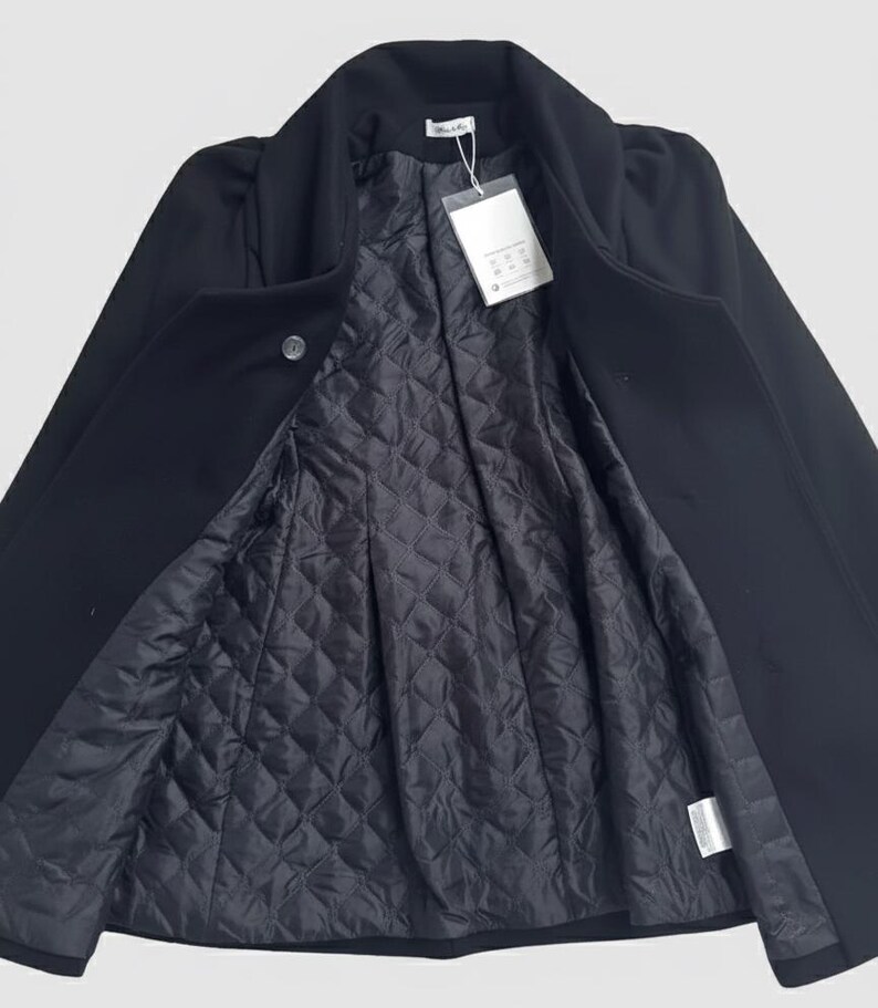 May include: A black coat with a quilted lining, open to display the interior. The coat has a classic collar and a single button closure. A white tag hangs from the inside of the coat.