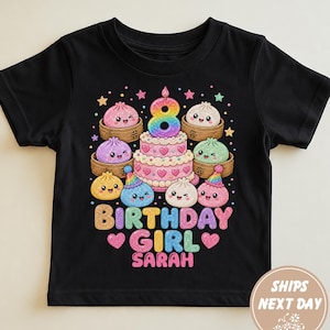 May include: A black short-sleeve t-shirt featuring a colourful graphic of a tiered birthday cake topped with the number 8, surrounded by various smiling dumplings in bamboo steamers, with the text BIRTHDAY GIRL SARAH in glittery letters.