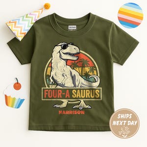 May include: Olive green t-shirt featuring a dinosaur wearing sunglasses, with the text "FOUR-A SAURUS" and a personalized name. The design includes a retro sunset and palm trees. A party hat and cupcake are in the background.