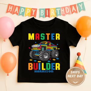 Könnte beinhalten: Schwarzes T-Shirt mit einer farbenfrohen Grafik eines Monster Trucks aus Spielzeugblöcken. Die Worte "MASTER BUILDER" sind in Blockbuchstaben dargestellt, darunter der Name "Harrison". Ballons und ein Geburtstagsbanner sind im Hintergrund.