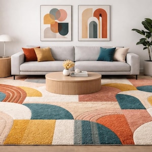 Può includere: Un soggiorno con un divano grigio, cuscini colorati e un tavolino rotondo in legno. Un grande tappeto con un motivo geometrico nei toni dell'arancione, verde acqua e giallo. Due opere d'arte astratte sono appese sopra il divano.