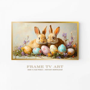 Puede incluir: Impresión de arte digital enmarcada que presenta dos conejos marrones rodeados de huevos de Pascua y flores coloridas. La obra de arte tiene un estilo suave y pictórico con un marco dorado. El texto en la parte inferior dice "FRAME TV ART".